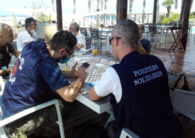 un volontaire de Pompiers Solidaires assis à table avec un libanais en train de travailler